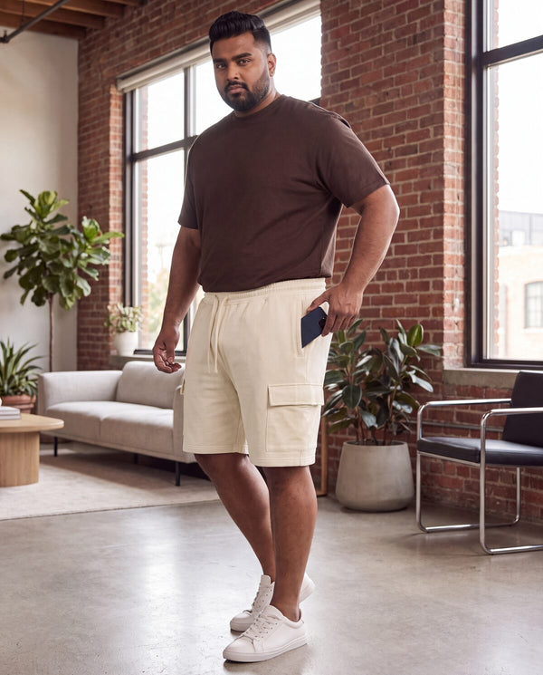 Plus-size man at home sliding a phone into cream FFlirtyGo cargo shorts