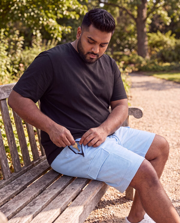 Plus-size man seated on a park bench in sky blue FFlirtyGo cargo shorts